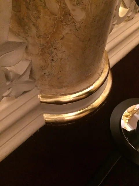 Close-up of gold leaf applied around the curved base of a faux-marble hotel column